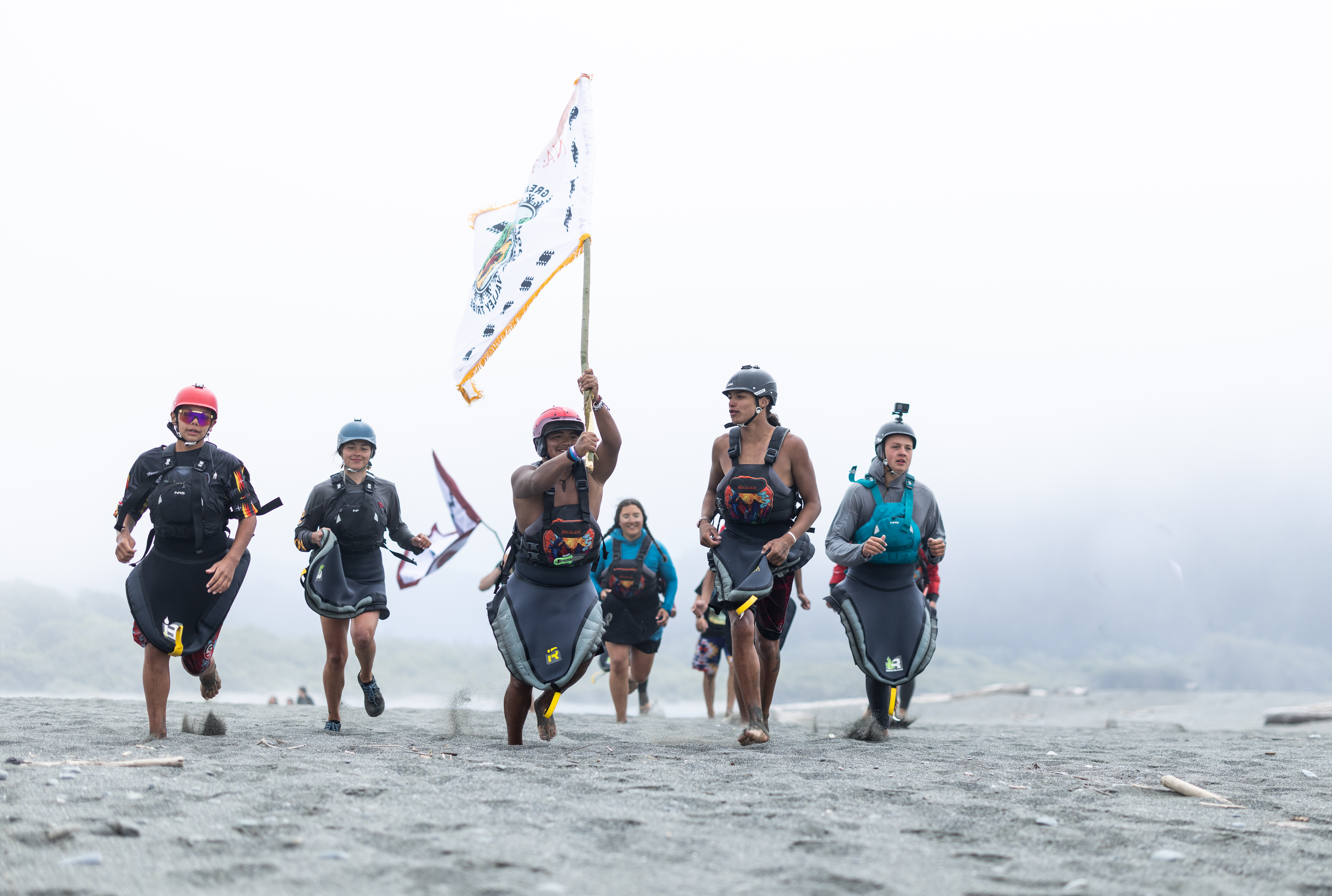 Young people run down a beach while holding a flag
